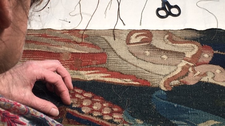 Hands of a conservator as they repair stitching on a tapestry