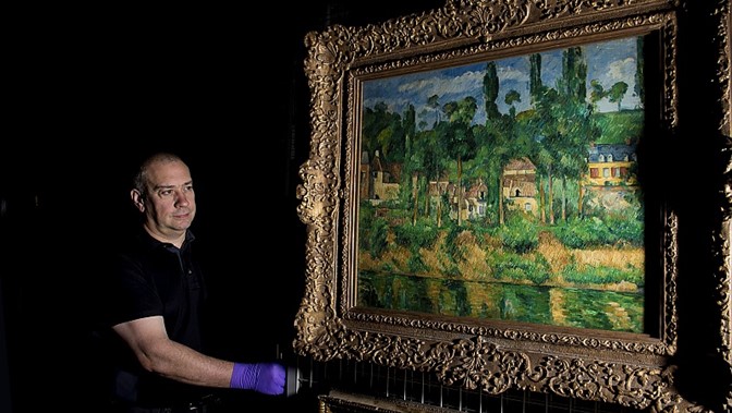 curator wearing gloves holds one of the French paintings from the Burrell Collection that will go on tour to Marseilles and cities across Japan