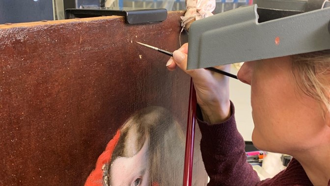 painter holds a paintbrush close to a painting of a child