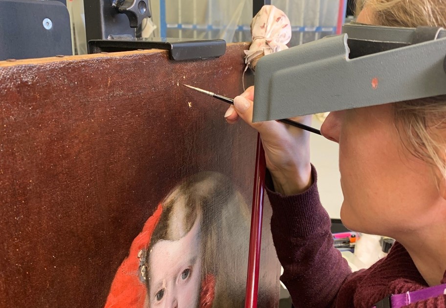 painter holds a paintbrush close to a painting of a child