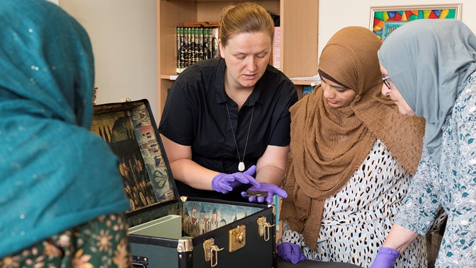 Image shows a curator wearing gloves showing off items from the Burrell Collection to woman from the local community